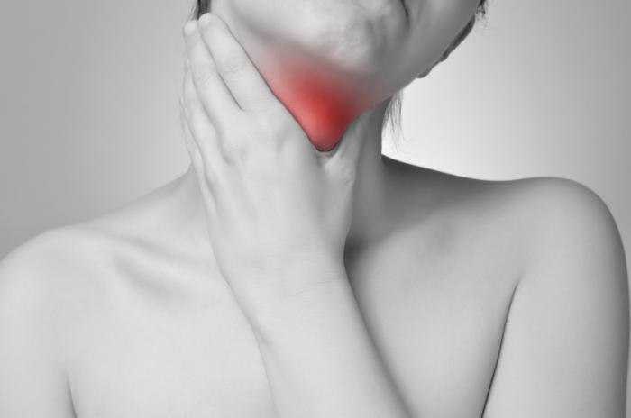 A woman is holding her red glowing throat.